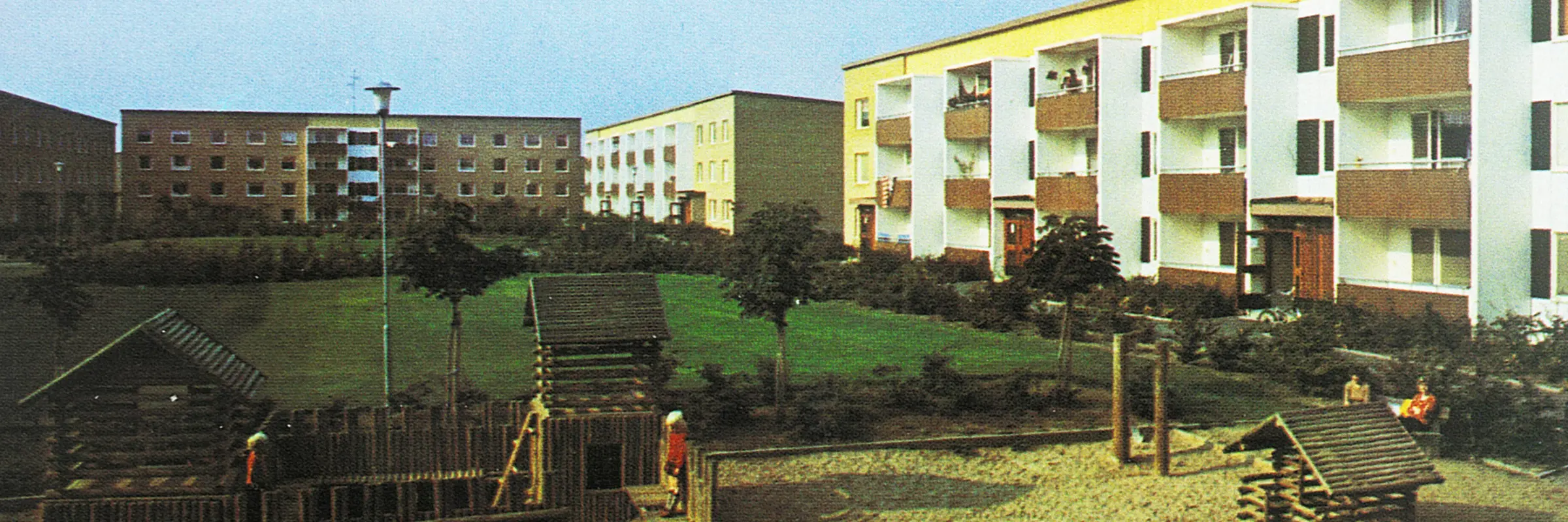 Bild tagen 1974 på hus på Gamlegården med en stor grön gräsmatta och lekplats i mitten av gården